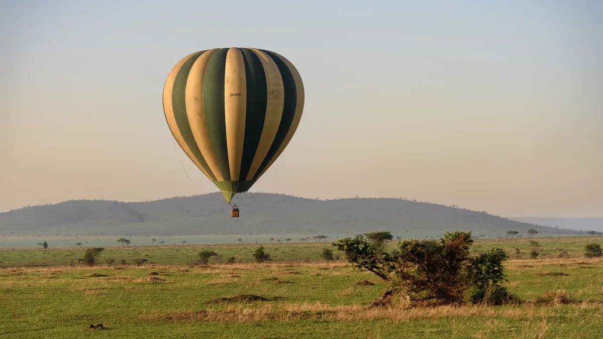 A striped hot air balloon over the Serengeti plains at dawn on a balloon flight added to Serengeti safari packages