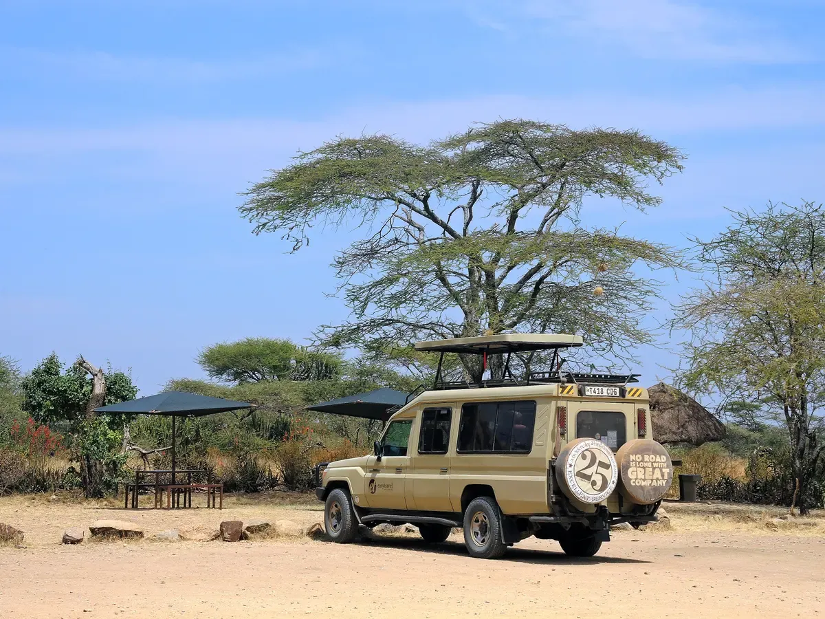 A safari vehicle with its roof raised under an acacia in Serengeti National Park, the kind of 4x4 used on Serengeti safari packages